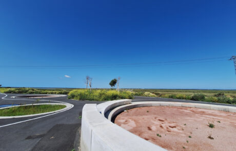 Rotonda con modernos elementos urbanos de hormigón curvados, delimitando zonas verdes en un paisaje natural.