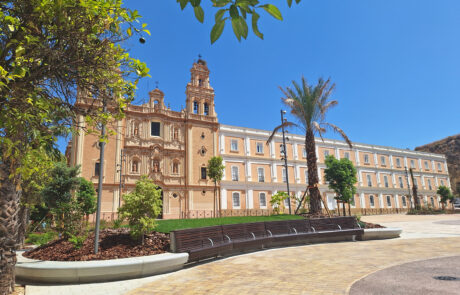 Moderno mobiliario urbano de hormigón prefabricado en una plaza soleada con un edificio histórico.