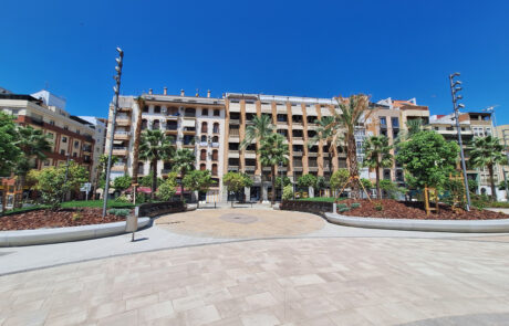 Plaza urbana con mobiliario urbano de hormigón, bancos y edificios residenciales.