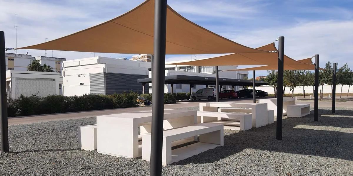 Conjunto de mesas y bancos de hormigón con toldos tensados como equipamiento urbano.