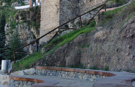 Banco curvo de piedra y madera con barandilla de madera al fondo como elementos de equipamiento urbano.