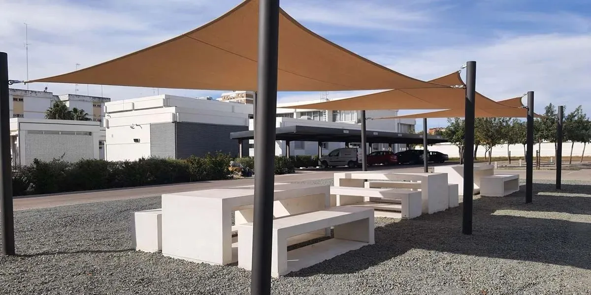 Conjunto de mesas y bancos de hormigón con toldos tensados como equipamiento urbano.